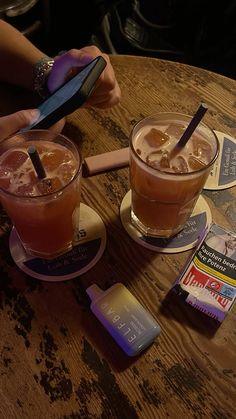 two drinks are sitting on the table and one has a cell phone in its hand