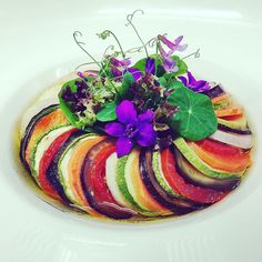 a white plate topped with sliced up vegetables and purple flowers on top of each other