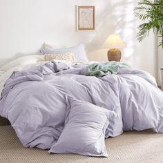 an unmade bed in a bedroom next to a lamp and potted palm tree