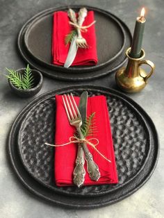 two black plates with red napkins and silverware on them, next to a candle