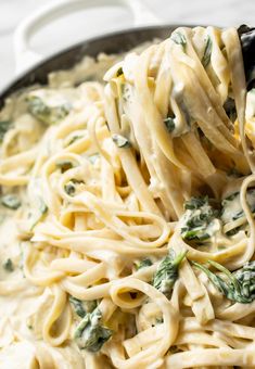 a pasta dish with spinach and cheese being stirred by a ladle over it