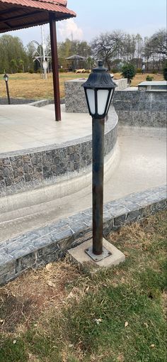 a lamp post sitting on the side of a road next to a stone wall and grass