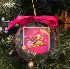 an ornament hanging from a christmas tree with a pink ribbon around it's edge