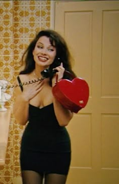 a woman is talking on the phone and holding a heart shaped box in her hand