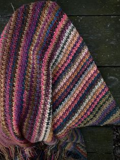 a multicolored crocheted shawl draped over a wooden surface