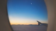 an airplane window with the view of clouds and a half moon in the sky above