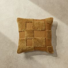 a brown pillow with squares on it sitting on top of a white carpeted floor