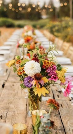 a long wooden table topped with vases filled with flowers next to glasses and candles