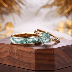 two gold rings with green stones sitting on top of a wooden box next to each other