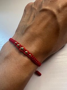 a person's arm with a red bracelet on it and two gold beads attached to the wrist