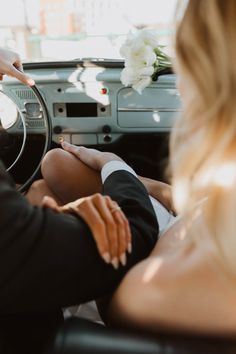 a man and woman sitting in the drivers seat of a car, holding hands on the steering wheel