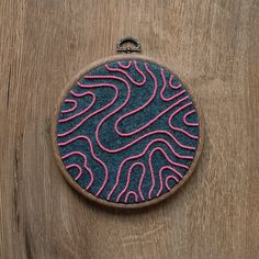 a blue and pink embroidered piece on a wooden surface with an oval shaped object in the middle