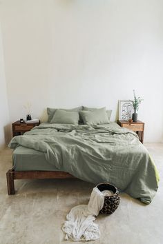 an unmade bed in a white room with green sheets and pillows on the floor