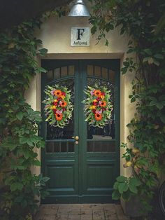 a green door with two wreaths on the front and side of it, surrounded by greenery