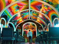 a man is walking down the aisle in a brightly colored room with rows of chairs