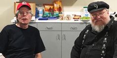 two older men sitting next to each other in a kitchen