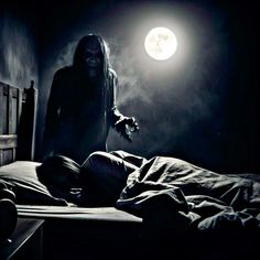 a person standing over a bed in a dark room with a full moon behind them