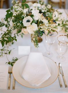 the table is set with white flowers and silverware, along with gold rimmed glasses