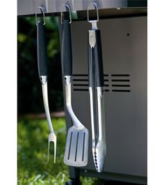 three cooking utensils hanging from the side of a grill