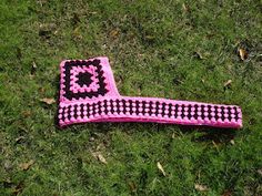 a pink and black crocheted object laying in the grass