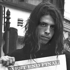 a man with long hair holding up a sign that says west end final street fair