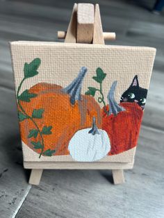 an easel with a painting of pumpkins and a cat on it