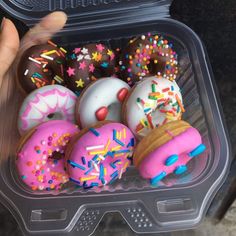 a plastic container filled with lots of donuts covered in sprinkles and frosting