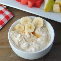 a bowl of fruit dip with bananas and watermelon slices in the background on a wooden table