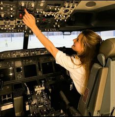 a woman is sitting in the cockpit of an airplane and pointing to the control panel