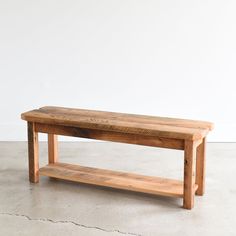 a wooden bench sitting on top of a cement floor next to a white wall in an empty room