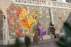 a man and woman standing in front of a building with a mural on it's side