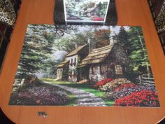 a wooden table with a puzzle on top of it and a painting of a cottage in the background