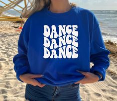 a woman wearing a blue sweatshirt with the words dance dance on it in white letters