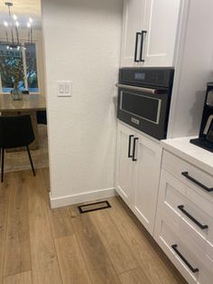 a kitchen with white cabinets and black appliances on the counter top, next to a dining room table