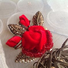 a red rose brooch sitting on top of a white table cloth covered in beads