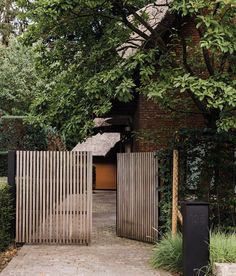 a wooden gate in front of a brick building surrounded by greenery and trees on either side