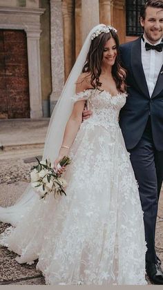 the bride and groom are walking together in front of an old building wearing tuxedos