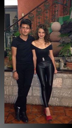 a man and woman standing next to each other in front of a stair case with potted plants