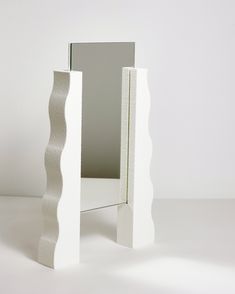 a small white table with a mirror on it's side and an object in the middle