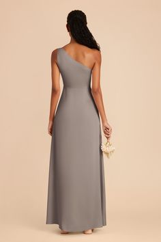 a bridesmaid in a grey one - shoulder dress holding a bouquet and looking back