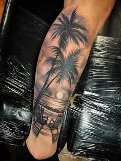 a person with a palm tree tattoo on their arm and leg, next to a chair