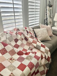 a couch with a quilt on it next to a window covered in pillows and blankets