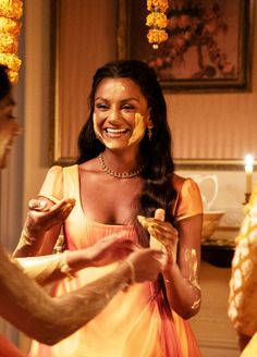 a woman in an orange dress smiles as another man holds something up to her face