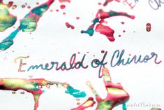 the word emeraldl of chaos written in ink on white paper with multicolored paint splattered all over it