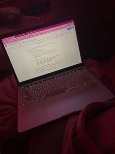 an open laptop computer sitting on top of a red blanket covered bed in the dark