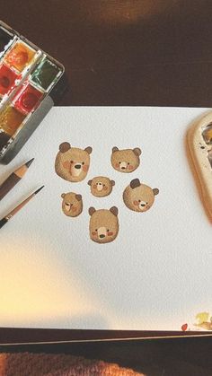 the bear faces are drawn on paper next to some watercolors and paintbrushes