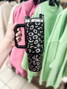 a person holding a black and white leopard print coffee cup in front of clothing racks