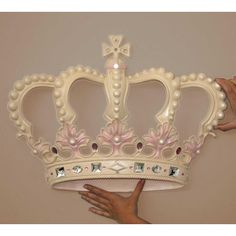 a hand holding a large white crown with pearls on the sides and pink flowers on the side