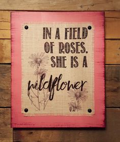 a pink sign with the words in a field of roses, she is a wildflower