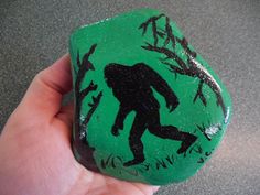 a hand holding a rock with a drawing of a bigfoot on it's side